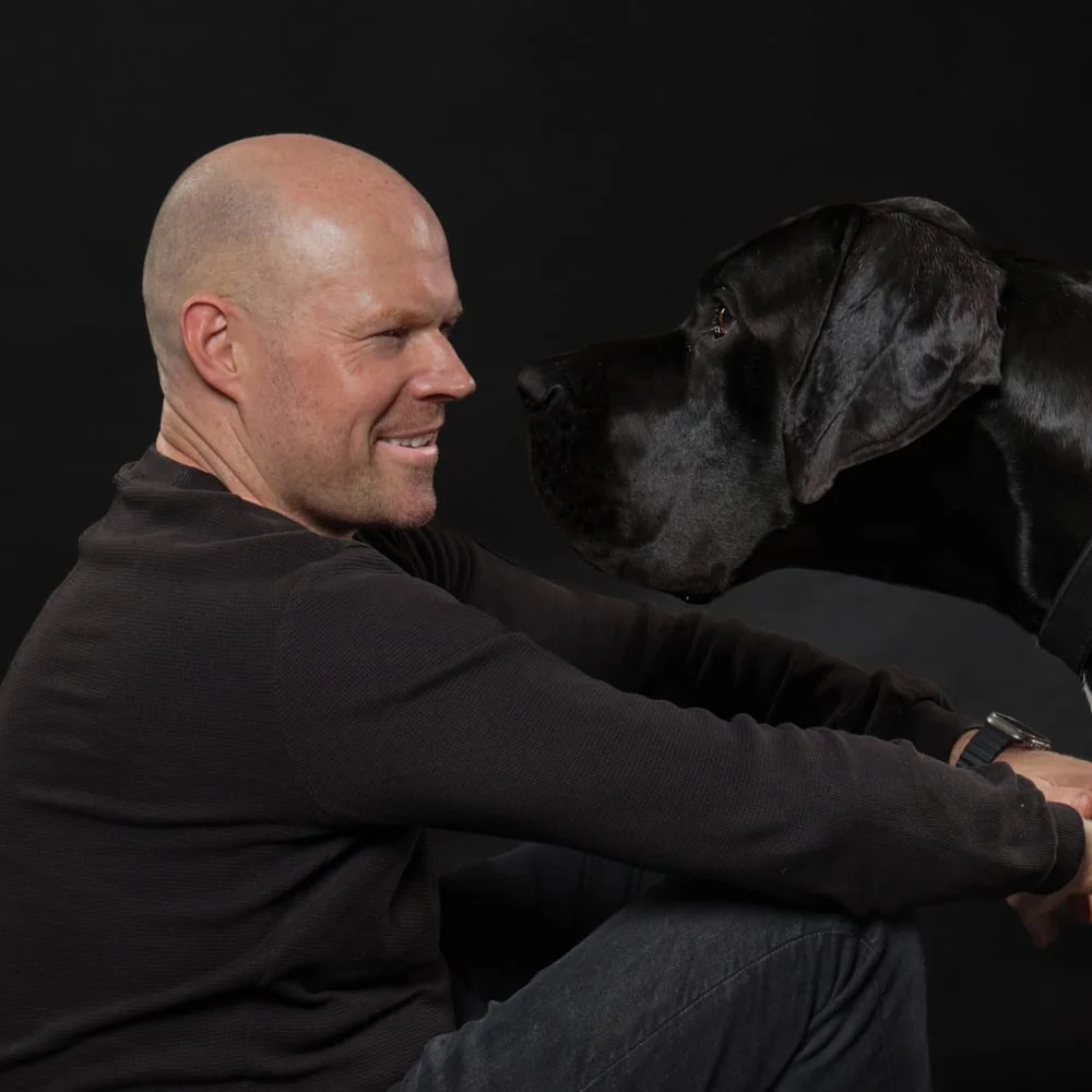 Tim Kahrmann, der Gründer von Tonight, sitzt mit seinem schwarzen Hund vor einem dunklen Hintergrund