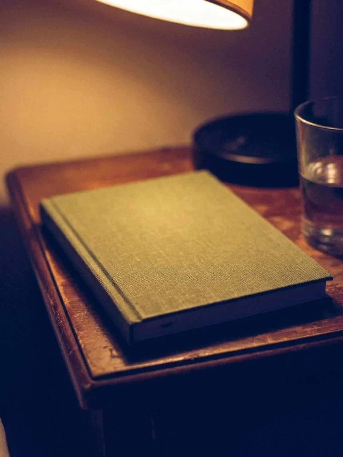 Un diario de lino cerrado descansando sobre una mesa de noche bajo una lámpara cálida.